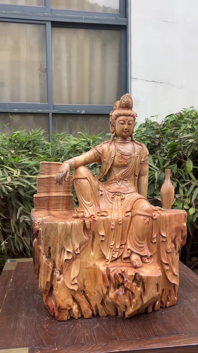 Hand-carved wooden Guanyin statue in a relaxed posture.